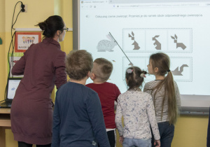 nauczycielka z dziecmi stoi przed tablicą multimedialna i rozwiązują zadanie o zajączku